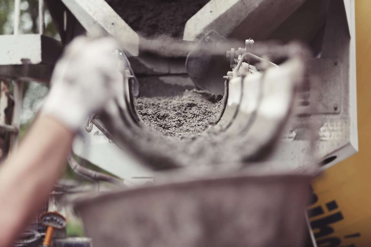 A construction worker pours and levels wet cement concrete on an active residential building site