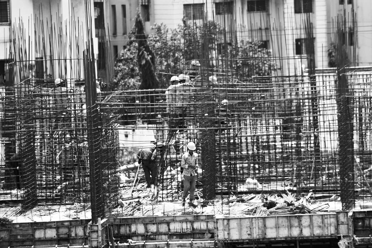 Workers in hard hats tying steel reinforcement for RCC columns at an Indian building site