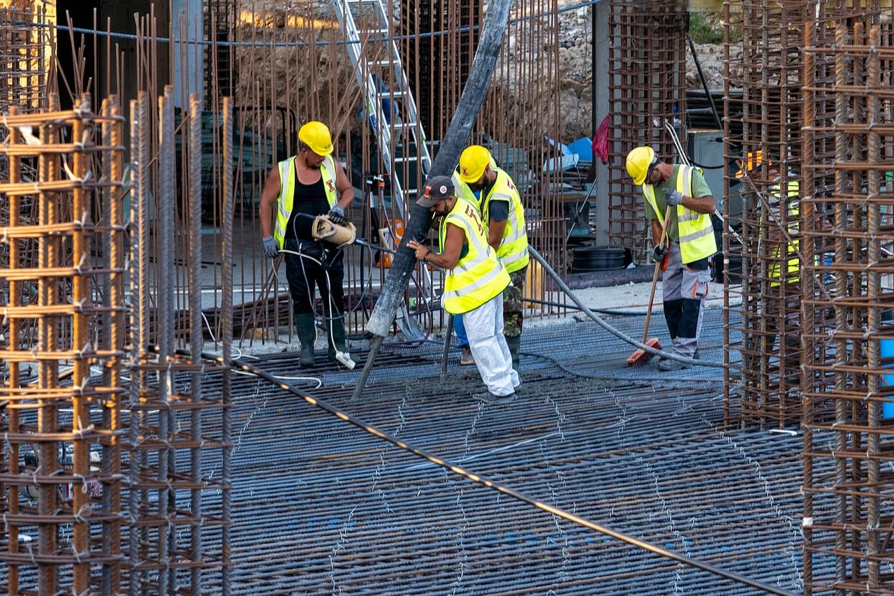 Construction crew pouring concrete over a steel reinforcement mat between column cages